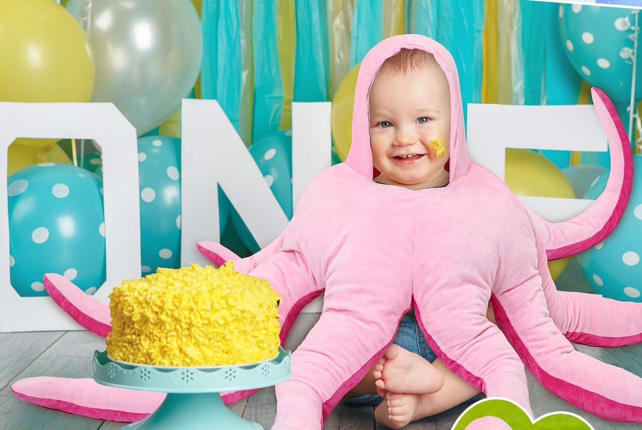 Smiling baby in the octopus costume beside a yellow first birthday cake